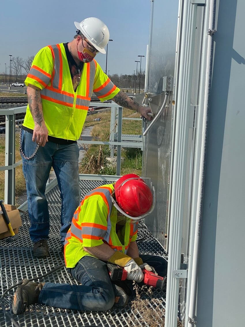 A Couple Of Men Standing Next To Each Other Wearing Safety Gear